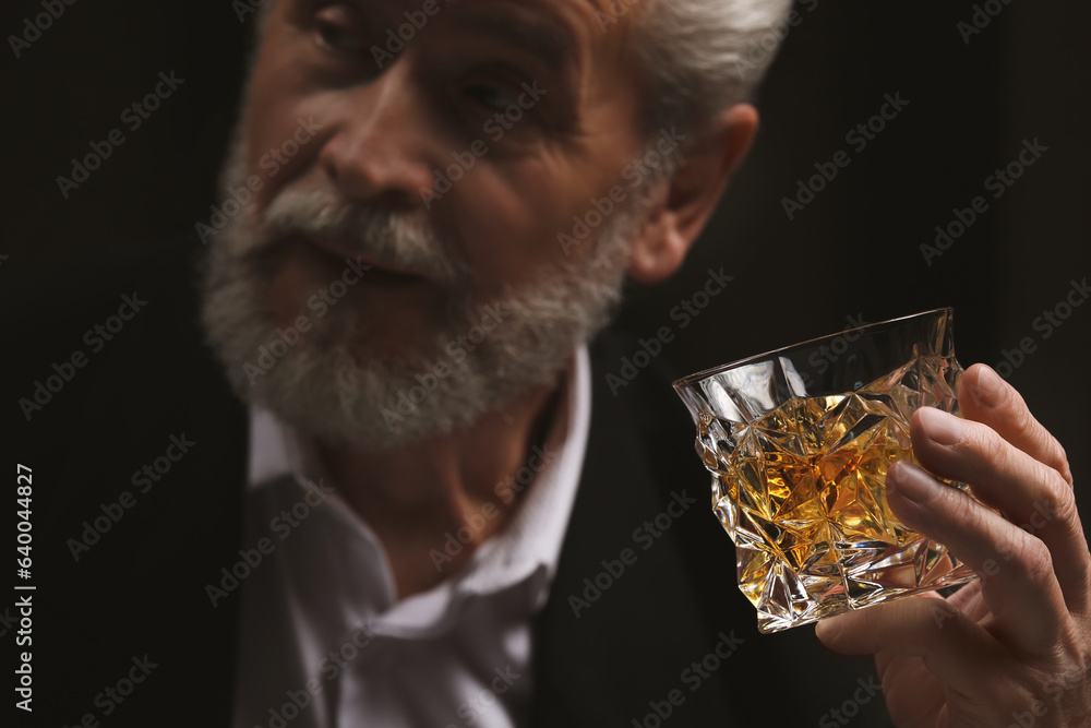 Man in suit holding glass of whiskey with ice cubes on black background, selective focus Man in suit holding glass of whiskey with ice cubes on black background, selective focus