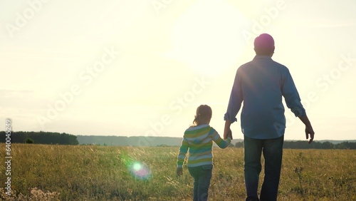 cheerful grandfather happily guides his granddaughter by hand walk through park together. enjoy holding hands strolling through park  creating joyful atmosphere for entire family. warm summer evening