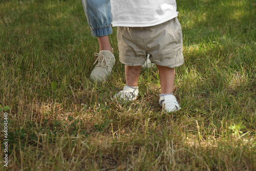 Mother supporting daughter while she learning to walk outdoors, closeup. Space for text