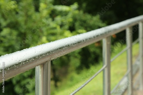 Metal handrail with water drops outdoors, closeup. Rainy weather