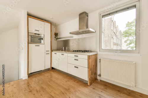 a kitchen area with wood flooring and white cupboards on either side of the window looking out onto the street