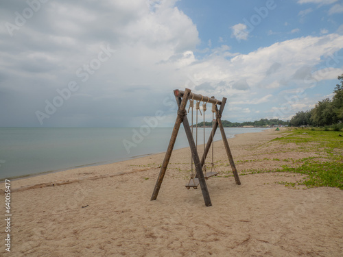 wooden swing tied with rope by the beach. beautiful tropical nature landscape. overlooking the bright green sea far and wide. the sky is cloudy with rain, and some are falling into the sea.