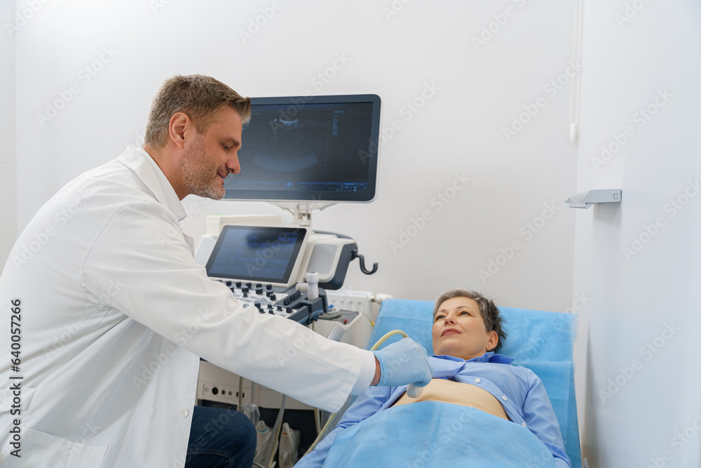 Middle aged woman patient lying on bed and having ultrasound examination of abdomen in clinic Middle aged woman patient lying on bed and having ultrasound examination of abdomen in clinic