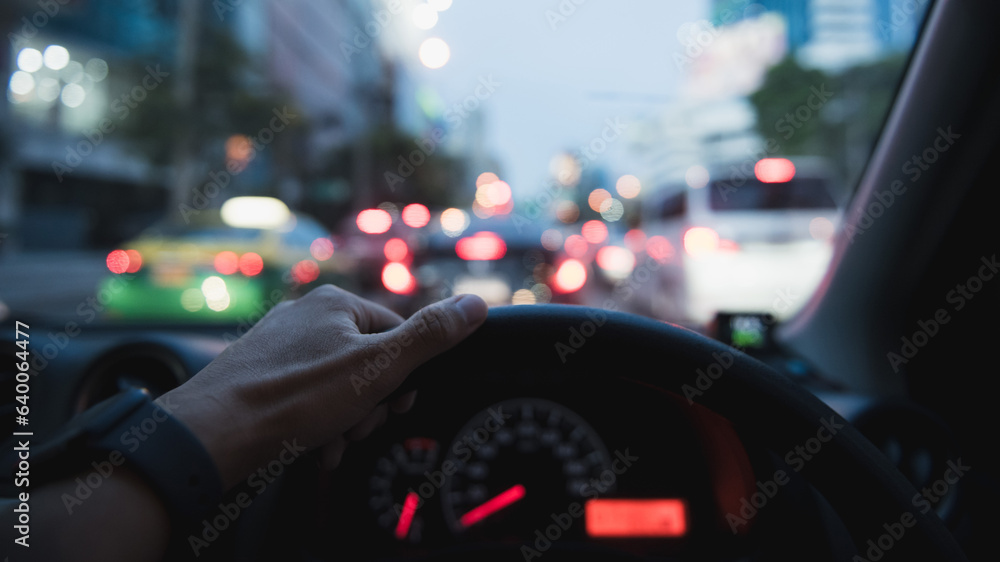 Close up image of young man hand holding on steering wheel driving car on the traffic jam in the big city with bokeh of car light.