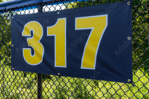 Photography 317 foot ft baseball field distance sign in yellow and black mounted on the black vinyl outfield fence