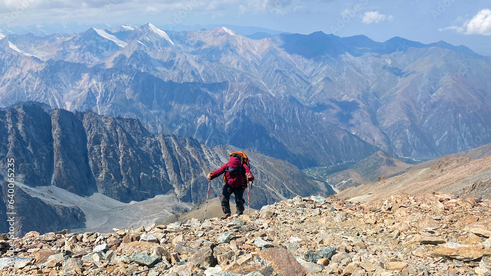 Active summer vacation. A tired lonely tourist with trekking poles climbs uphill. Ala Archa National Park. View from the height of the mountains