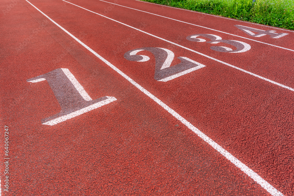 Image of an old red running track lane numbers, 1 through 4, with white lane lines and other markings.	