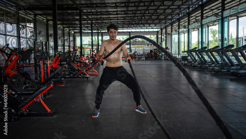 Man doing battle ropes exercise in a fitness gym. Shirtless fitness young sports man training .work out healthy. exhausted, tired out. struggle .difficult