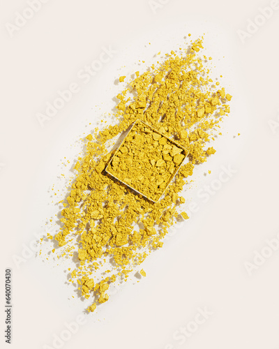 Yellow eye shadow, top view broken swatch of eye shadow powder on beige background. Eyes makeup powder texture. Yellow crushed make up powder sample, Female cosmetic and beauty product