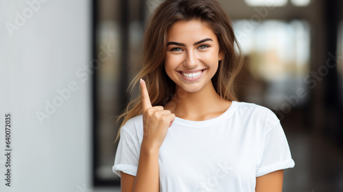 woman with pleasant smile in white blank t-shirt pointing with index finger alone or up, generated by AI
