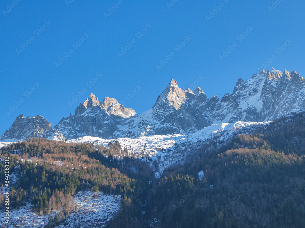 Scenic view of white snowcapped mountain peaks in Charmonix, French Alps, France, Europe. Snowy summits and dark green coniferous trees hill and blue winter sky. Chamonix Needles chain near Mont Blanc