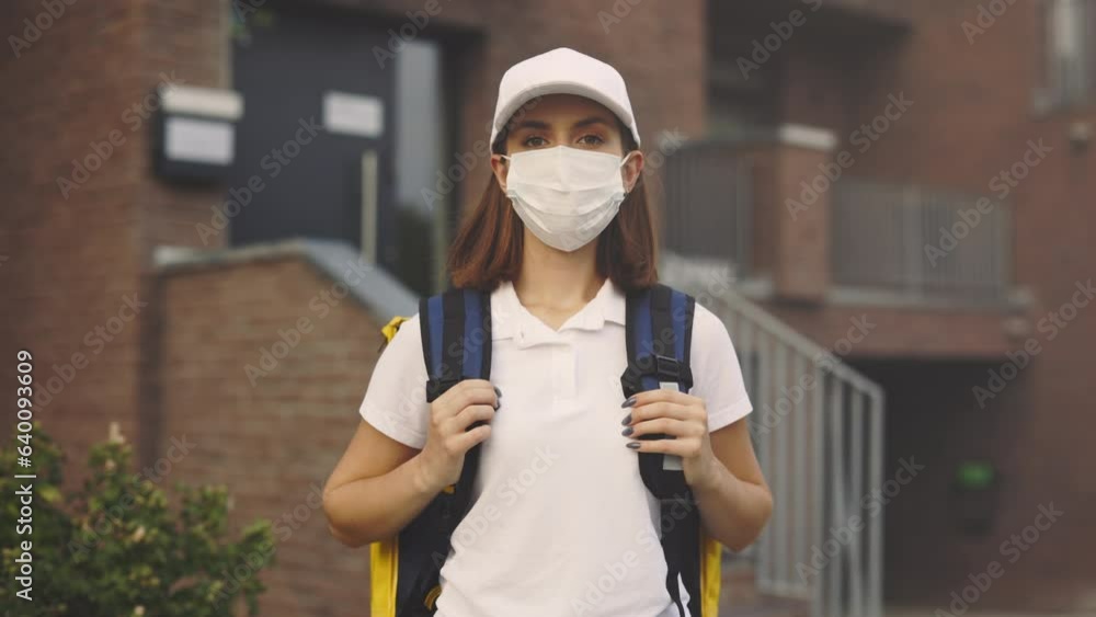 Portrait of the Caucasian Woman Courier in Protective Mask Standing Near the Building. Fast Safe Delivery. Postal Lady Home Delivery Looking at Camera. Woman Worker Delivery While Pandemic Portrait of the Caucasian Woman Courier in Protective Mask Standing Near the Building. Fast Safe Delivery. Postal Lady Home Delivery Looking at Camera. Woman Worker Delivery While Pandemic