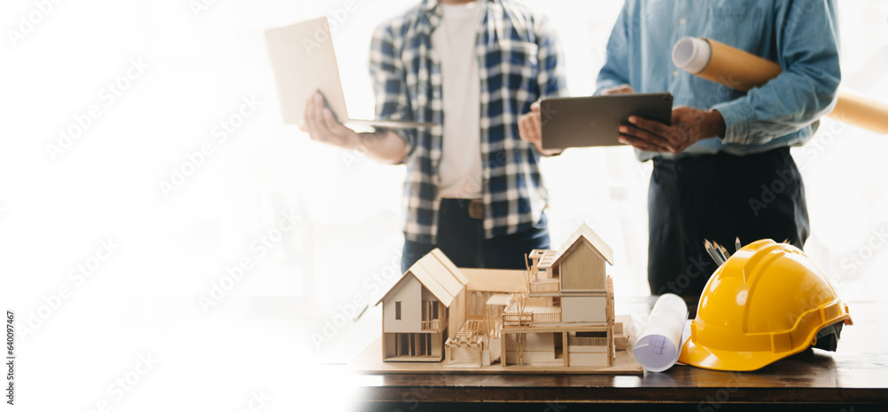 Engineer desk with object paper and tablet with blurry engineer teamwork hardworking to consults about their building project.. Engineer desk with object paper and tablet with blurry engineer teamwork hardworking to consults about their building project..