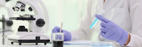 Fotografia A woman in front microscope and blue reagent in test tube