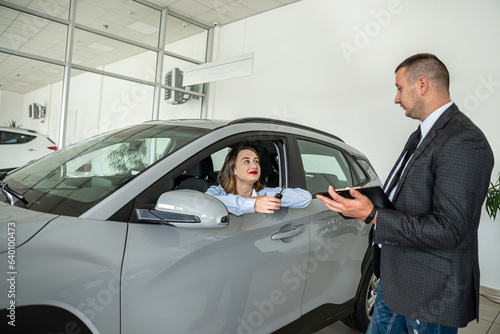 Young female business client talking with a sales man in a car showroom © RomanR
