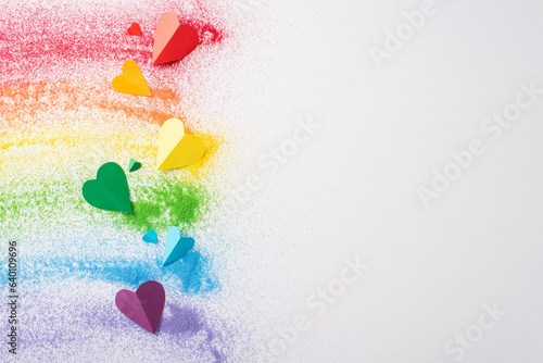 Fototapeta Naklejka Na Ścianę i Meble -  Top view of sand flag celebrates LGBT history month. Colorful sand forms a rainbow flag and small hearts on white, with an open circle for empowering and inclusive messages