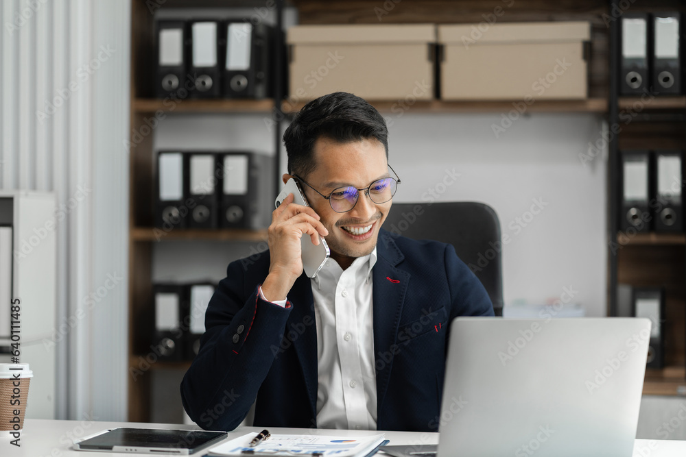 Smiling Asian young freelancer working from home remotely.He is talking on the phone. Smiling Asian young freelancer working from home remotely.He is talking on the phone.