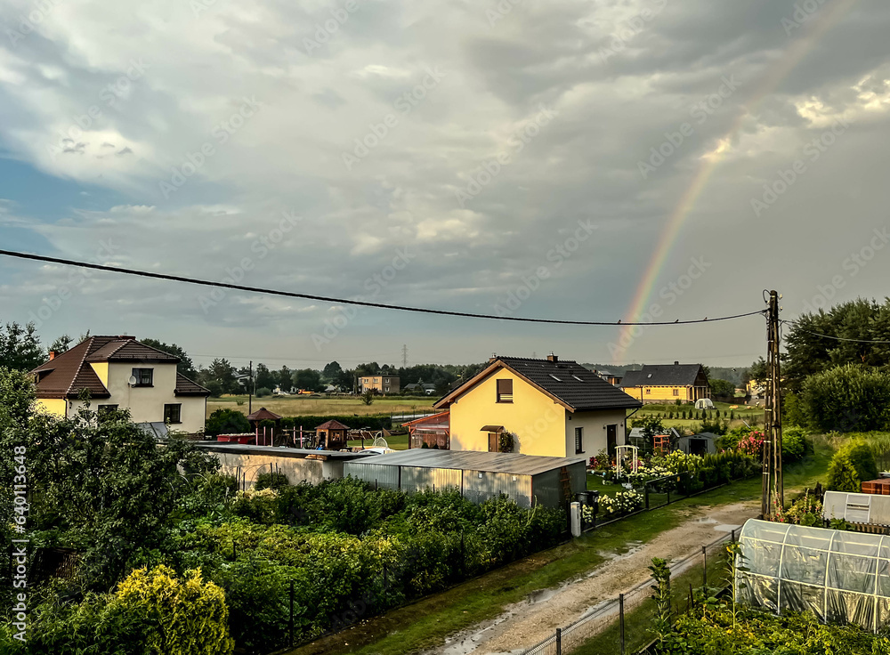 Rainbow, over trees and village buildings, in the sky after the rain Rainbow, over trees and village buildings, in the sky after the rain