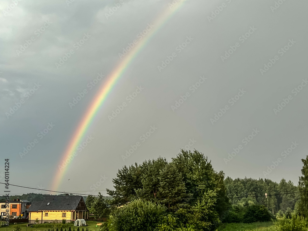 Rainbow, over trees and village buildings, in the sky after the rain