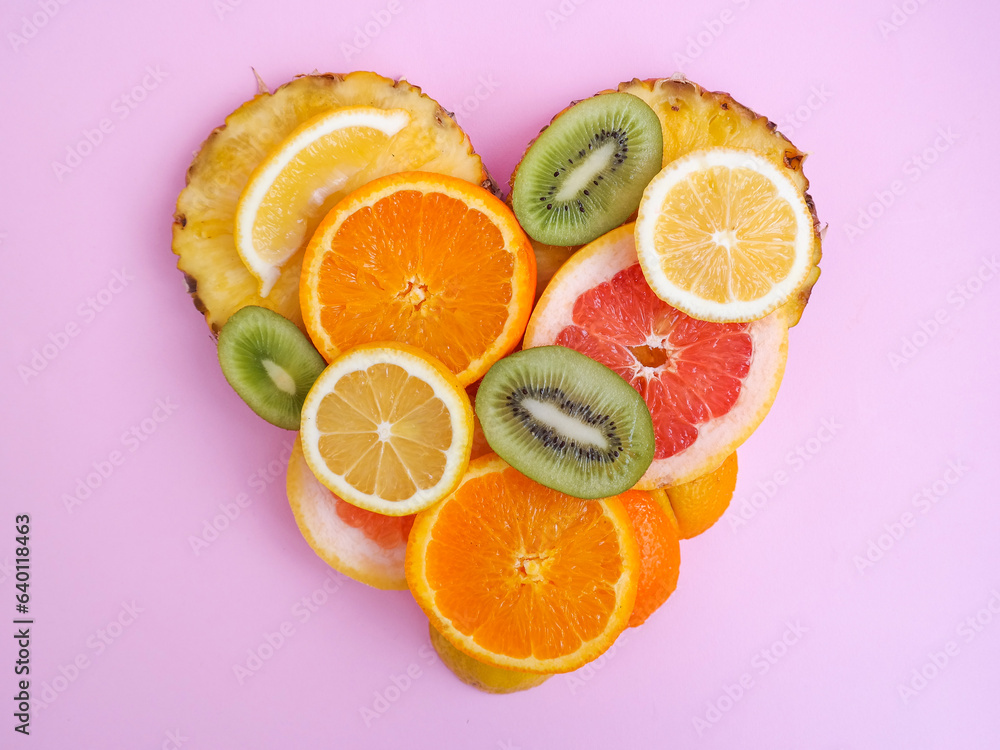 Fruit heart made of pineapple, grapefruit, orange, lemon and kiwi slices against bright pink background. Copy space. Creative summer idea. Minimal fruit concept.