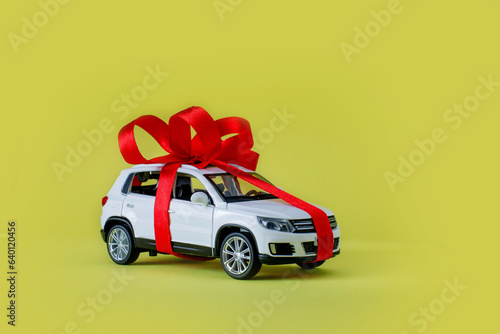 White model car with bow on a yellow background. Car as gift, surprise