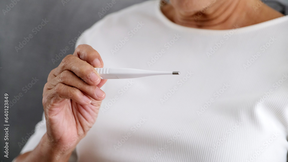 Close up of old woman hand holding thermometer at home, Flu asia fmale holding a digital thermometer when measures the temperature, People get fever, infection from virus check body temperature Close up of old woman hand holding thermometer at home, Flu asia fmale holding a digital thermometer when measures the temperature, People get fever, infection from virus check body temperature
