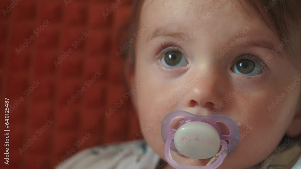 a small newborn sits on the couch with a pacifier in his mouth. happy family childhood dream concept. a little child with a purple pacifier sits and looks at the lifestyle camera close-up a small newborn sits on the couch with a pacifier in his mouth. happy family childhood dream concept. a little child with a purple pacifier sits and looks at the lifestyle camera close-up