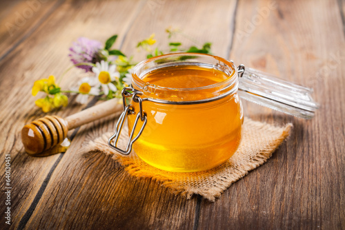 Glass jar with floral liquid honey, flowers and honey dipper. Copy space