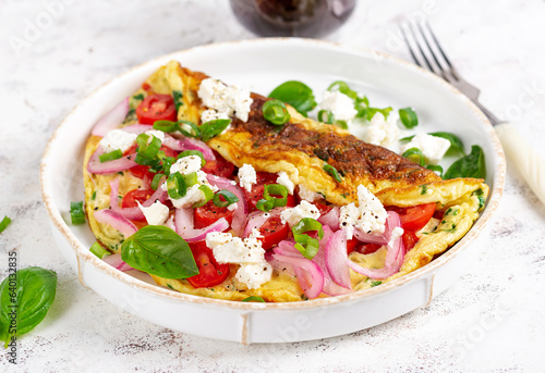 Omelette with tomatoes, feta cheese and red onion on white plate. Frittata - italian omelet.