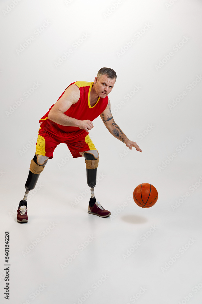 Attractive, confident, sporty man with prosthetic legs, disability with orange basketball ball in motion. Inclusive sport for people with disabilities.