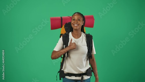 Woman tourist with backpack walks into a frame, shows a thumbs up smiling at the camera. Isolated on green background. photo