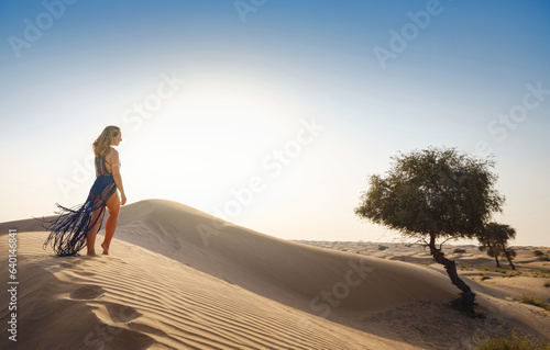 Desert adventure. Young arabian Woman in sexy boho blue makrame dress in sands dunes of UAE desert at sunset. The Dubai Desert Conservation Reserve, United Arab Emirates. photo