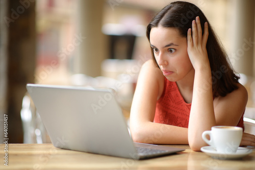Fotografie Perplexed woman checking laptop in a bar terrace