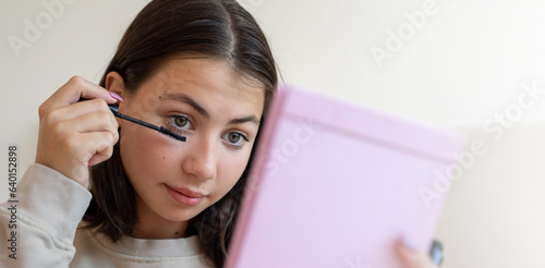 Obraz na płótnie Teenage girl putting makeup. Young woman looking at mirror and apply mascara on eyelashes in bedroom. Cosmetics for youth culture trend. Daily make-up. Copy space w salonie