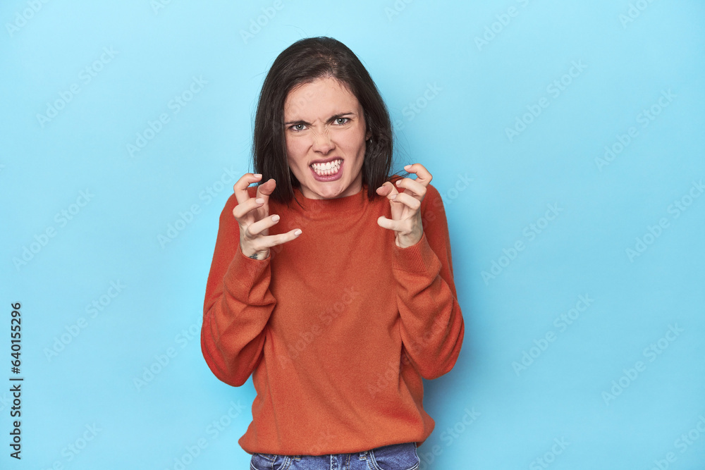 Young caucasian woman on blue backdrop upset screaming with tense hands. Young caucasian woman on blue backdrop upset screaming with tense hands.