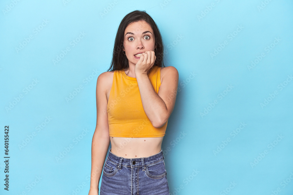 Young caucasian woman on blue backdrop biting fingernails, nervous and very anxious. Young caucasian woman on blue backdrop biting fingernails, nervous and very anxious.