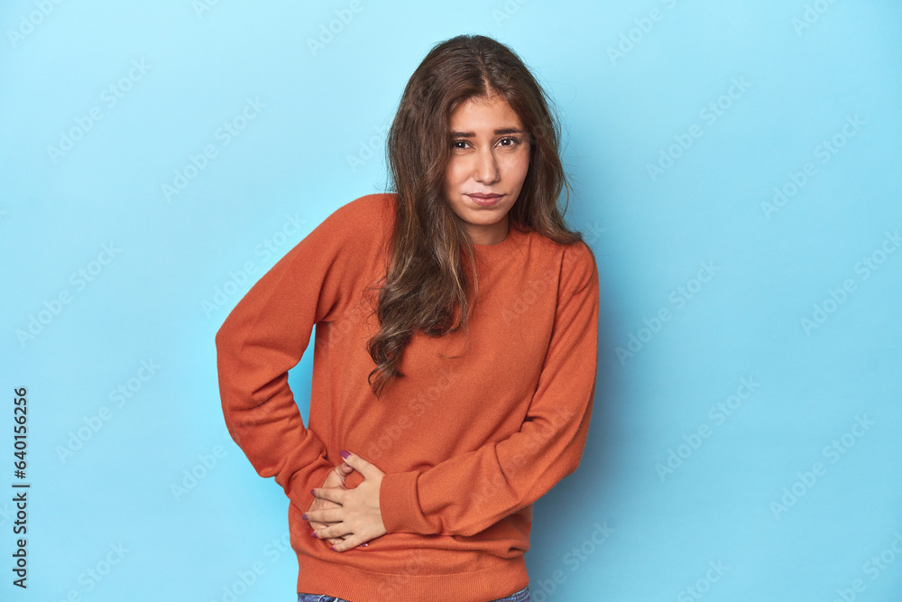Teen girl in vibrant orange sweater on blue having a liver pain, stomach ache. Teen girl in vibrant orange sweater on blue having a liver pain, stomach ache.
