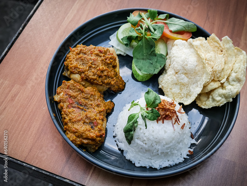 Ayam bakar Taliwang is a traditional roast chicken from Lombok Indonesia, isolated on a wooden background, served with vegetables. Spicy but tasty cuisine photo