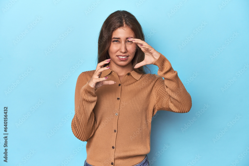 Teen girl in brown polo shirt on blue upset screaming with tense hands. Teen girl in brown polo shirt on blue upset screaming with tense hands.