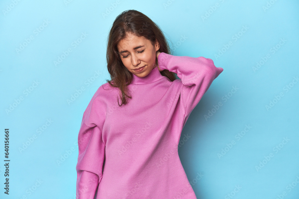 Teen girl in cozy pink sweatshirt on blue suffering neck pain due to sedentary lifestyle. Teen girl in cozy pink sweatshirt on blue suffering neck pain due to sedentary lifestyle.