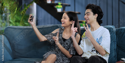Canvas Print Smiling Asian two friend sitting sofa taking funny faces selfie teen boy man hol