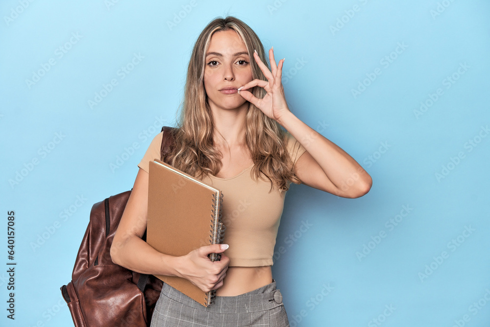 Blonde student with notebooks and backpack with fingers on lips keeping a secret. Blonde student with notebooks and backpack with fingers on lips keeping a secret.