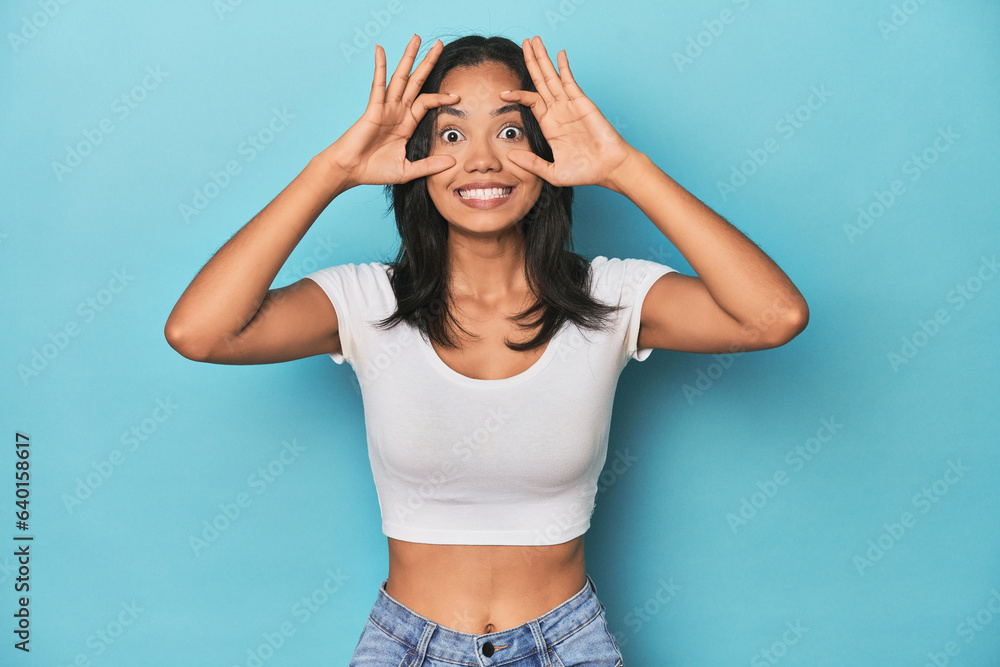 Filipina young woman on blue studio keeping eyes opened to find a success opportunity.