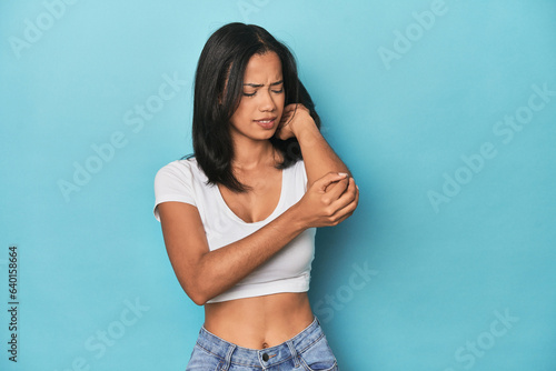 Filipina young woman on blue studio massaging elbow, suffering after a bad movement. © Asier