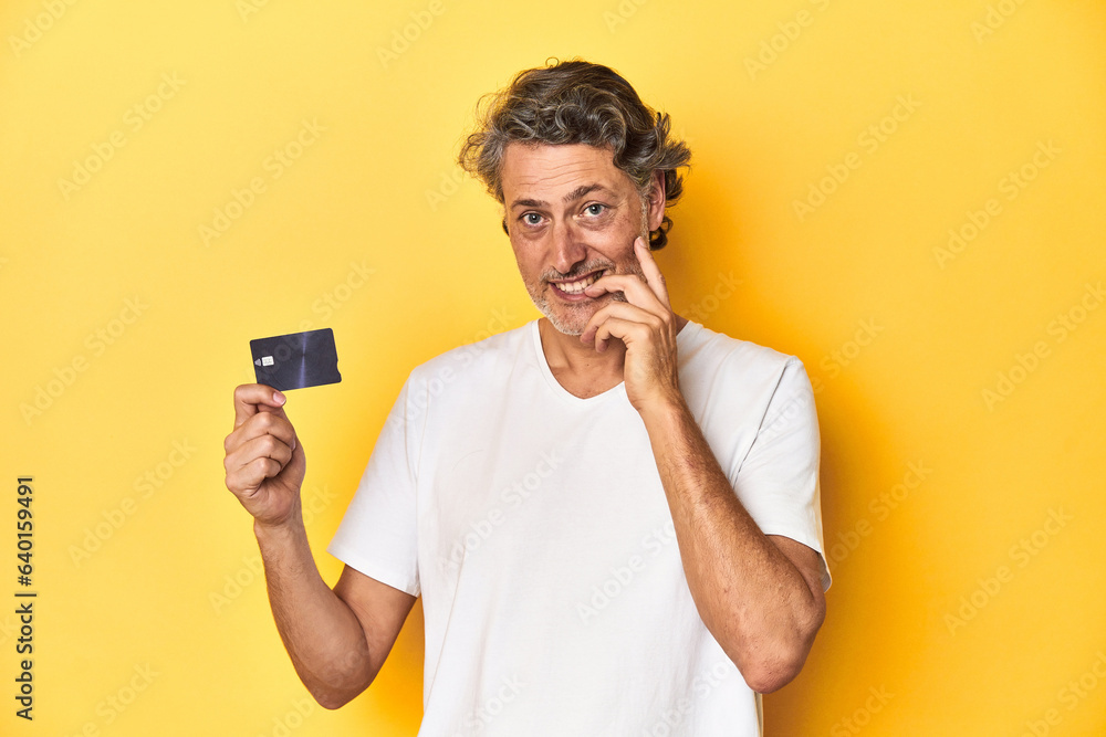Man holding a credit card, yellow studio backdrop relaxed thinking about something looking at a copy space. Man holding a credit card, yellow studio backdrop relaxed thinking about something looking at a copy space.