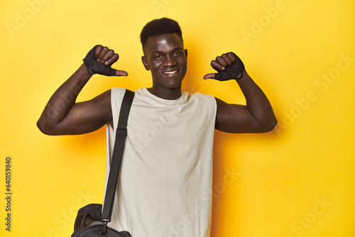 Fit African man with gym backpack on yellow studio background, feels proud and self confident, example to follow.
