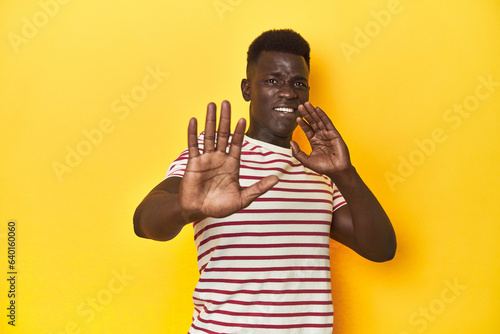 Stylish young African man on vibrant yellow studio background, being shocked due to an imminent danger