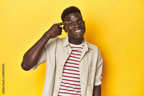 Stylish young African man on vibrant yellow studio background, showing a disappointment gesture with forefinger.