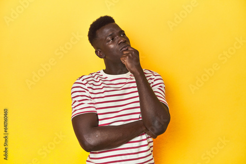 Stylish young African man on vibrant yellow studio background, thinking and looking up, being reflective, contemplating, having a fantasy.