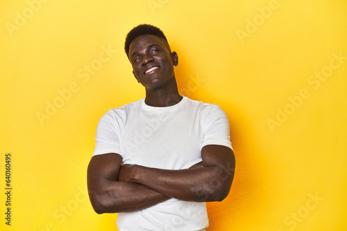 Stylish young African man on vibrant yellow studio background, dreaming of achieving goals and purposes